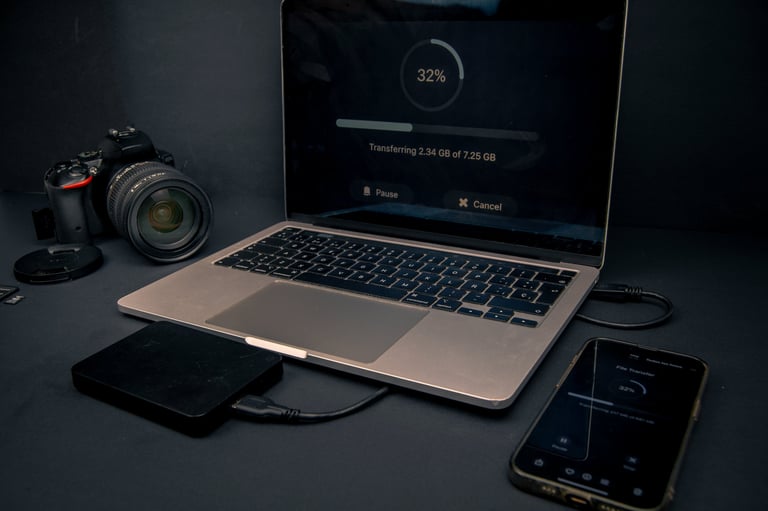 Laptop and smartphone showing file transfer progress with a camera and external hard drive. Backup, storage and data management workflow.
