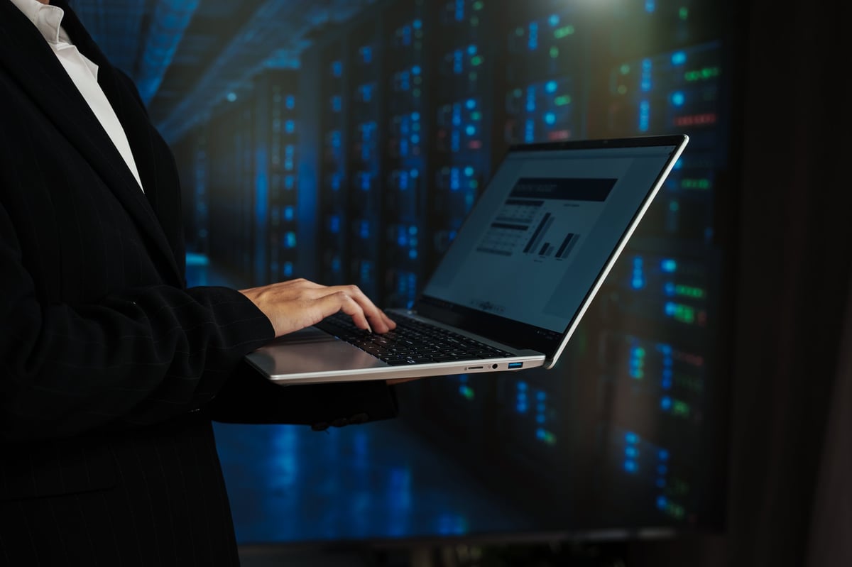 Business professional using laptop in server room with glowing data racks, cybersecurity and cloud computing concept, modern tech background with copy space.