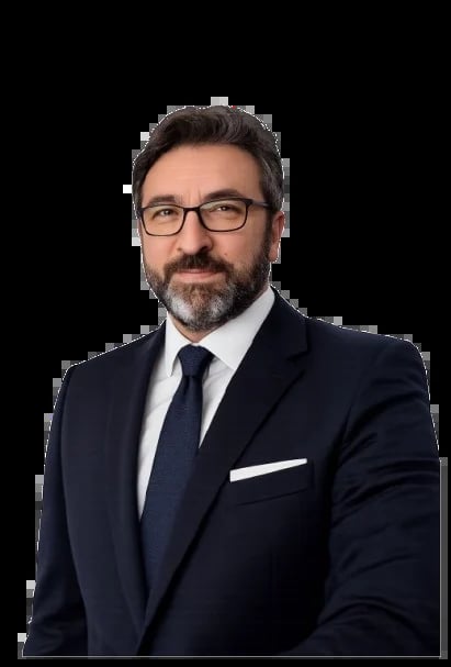 Professional headshot of a man with dark hair and beard wearing glasses, navy blazer, white shirt and navy tie against black background